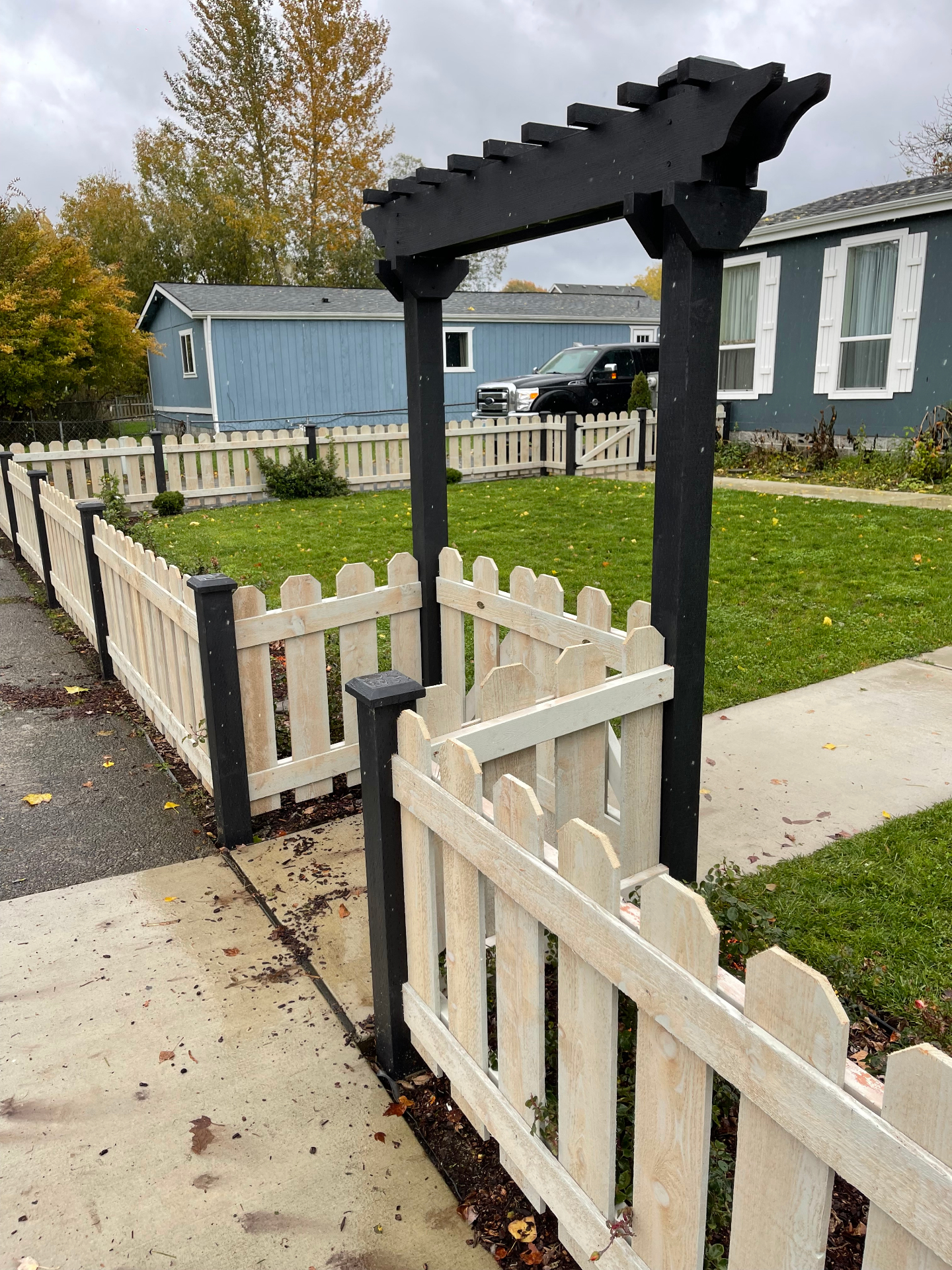 Black stained artisan trellis above picket fence gate
